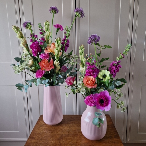 A spring arrangement in a matt pink ceramic vase featuring matthiola, tuberose, allium, roses, carnations, and anemones in fuchsia, apricot, yellow, and pink tones, styled in a natural Floramay design.