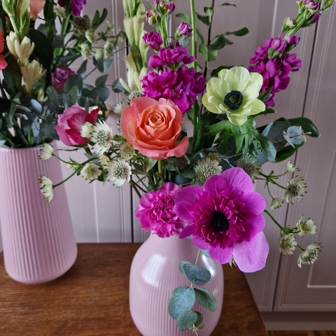 A spring arrangement in a matt pink ceramic vase featuring matthiola, tuberose, allium, roses, carnations, and anemones in fuchsia, apricot, yellow, and pink tones, styled in a natural Floramay design.