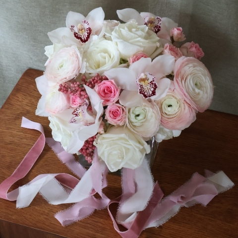A luxury cube‑vase arrangement with white hydrangea, pale pink Cloni ranunculus, pink spray roses, white roses, white cymbidium orchid heads and pink pepperberries.