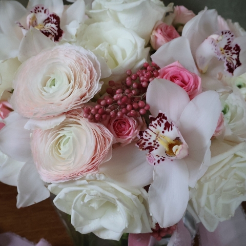 A luxury cube‑vase arrangement with white hydrangea, pale pink Cloni ranunculus, pink spray roses, white roses, white cymbidium orchid heads and pink pepperberries.