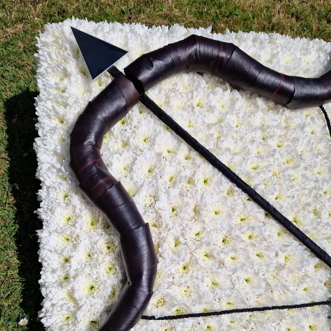 Bespoke funeral wreath with bow and arrow design made from black tie leaves on white chrysanthemum base