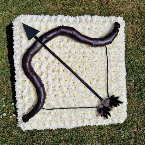 Bespoke funeral wreath with bow and arrow design made from black tie leaves on white chrysanthemum base