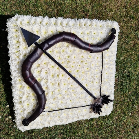 Bespoke funeral wreath with bow and arrow design made from black tie leaves on white chrysanthemum base