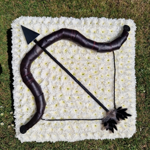 Bespoke funeral wreath with bow and arrow design made from black tie leaves on white chrysanthemum base