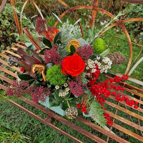 Christmas hat box arrangement with burnt orange roses, burgundy Skimmia, wax flower, ilex berries, pine, ivy berries, dried oranges, cinnamon sticks, and pine cones