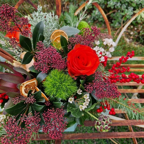 Christmas hat box arrangement with burnt orange roses, burgundy Skimmia, wax flower, ilex berries, pine, ivy berries, dried oranges, cinnamon sticks, and pine cones