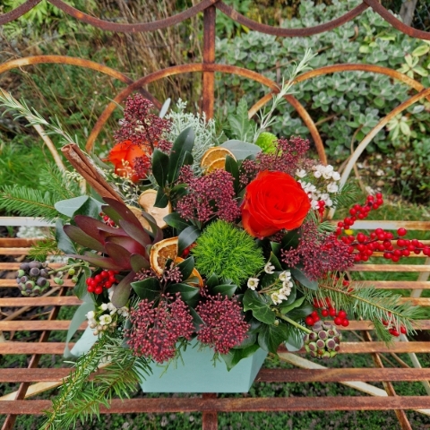 Christmas hat box arrangement with burnt orange roses, burgundy Skimmia, wax flower, ilex berries, pine, ivy berries, dried oranges, cinnamon sticks, and pine cones