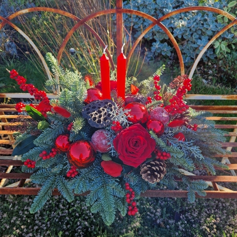 Crimson Eve Christmas centrepiece with red candles, deep red roses, fresh pine, waxed apples, pine cones, red baubles, and ilex berries