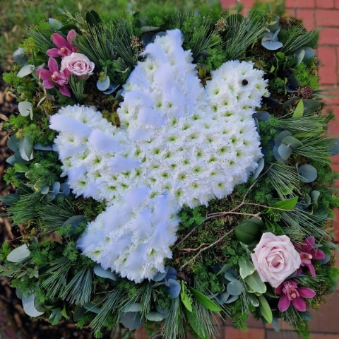 Dove-shaped funeral tribute with white chrysanthemums, nestled among foliage, leaves, and branches