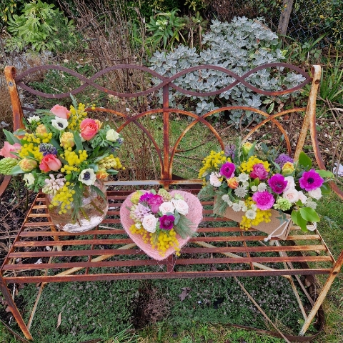 A spring arrangement in a jute trough-style box filled with mimosa, tulips, anemones, hyacinths, roses, allium, and carnations in apricot, fuchsia, yellow, and pink tones, arranged in a natural Floramay style.