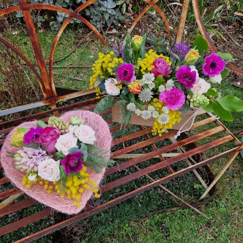 A spring arrangement in a jute trough-style box filled with mimosa, tulips, anemones, hyacinths, roses, allium, and carnations in apricot, fuchsia, yellow, and pink tones, arranged in a natural Floramay style.