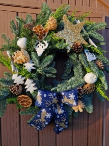 White and gold Christmas wreath with navy stag ribbon, gold sisal star, white coco trees, pine cones, lotus pods, waxed apples, and fresh pine on a moss ring.