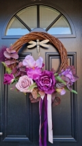 Handmade faux flower wreath in rich plum and pink tones, featuring flag iris, roses, and trailing ribbons, displayed on a black door with a metallic dragonfly ornament