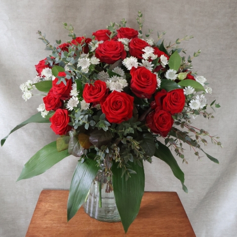A hand‑tied luxury Valentine’s bouquet of premium red roses, delicate white Astrantia and natural foliage, gift‑wrapped and presented in a kraft water‑holding bouquet box.
