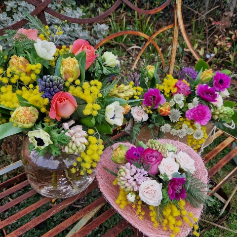A spring bouquet in a blush glass vase featuring mimosa, tulips, anemones, roses, and hyacinths in apricot, yellow, pink, and fuchsia tones, arranged in a loose, natural Floramay style.