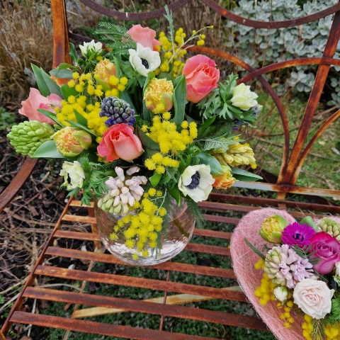 A spring bouquet in a blush glass vase featuring mimosa, tulips, anemones, roses, and hyacinths in apricot, yellow, pink, and fuchsia tones, arranged in a loose, natural Floramay style.