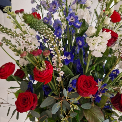 A bold statement arrangement of red, white and blue seasonal flowers, styled with height and movement and presented in a decorative urn.