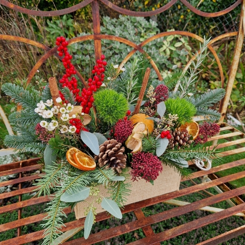 Winter arrangement in a hessian trough with pine, ilex berries, dried oranges, cinnamon sticks, pine cones, wax flower, and natural foliage.