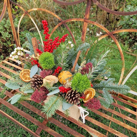 Winter arrangement in a hessian trough with pine, ilex berries, dried oranges, cinnamon sticks, pine cones, wax flower, and natural foliage.