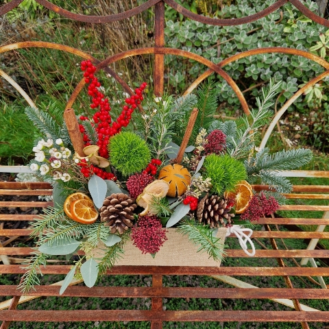 Winter arrangement in a hessian trough with pine, ilex berries, dried oranges, cinnamon sticks, pine cones, wax flower, and natural foliage.