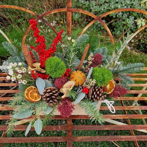 Winter arrangement in a hessian trough with pine, ilex berries, dried oranges, cinnamon sticks, pine cones, wax flower, and natural foliage.